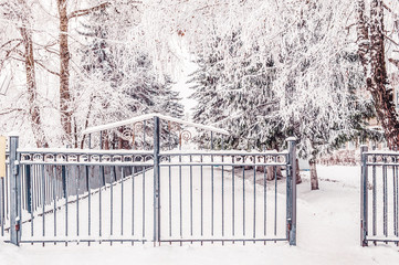 Metal fence with entrance gate along the snow-covered path. Winter Snow urban landscape