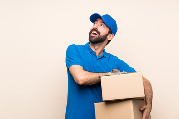 Delivery man with beard over isolated background looking up while smiling