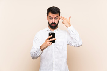 Young man with beard holding a mobile with problems making suicide gesture