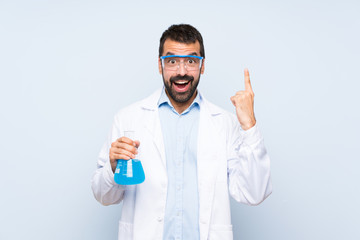 Young scientific holding laboratory flask over isolated background pointing up a great idea