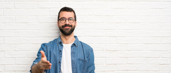 Handsome man with beard over white brick wall shaking hands for closing a good deal