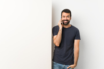 Young handsome man with beard holding a big empty placard keeping a conversation with the mobile phone