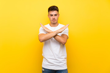 Young handsome man over isolated yellow background making NO gesture