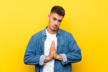 Young handsome man over isolated yellow background pleading