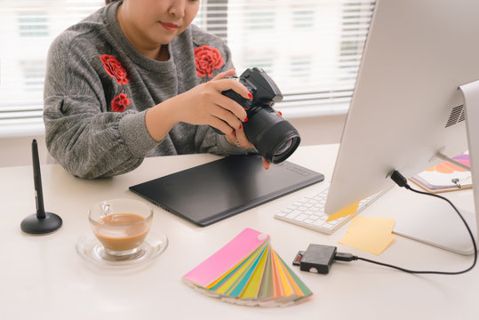 female freelancer photographer cheking photos on a digital camera while sitting at the table in workstation