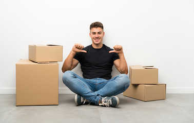 Handsome young man moving in new home among boxes proud and self-satisfied