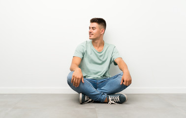 Young handsome man sitting on the floor looking to the side