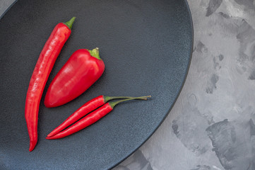 Colorful mix of the freshest and hottest chili peppers and Bulgarian colored pepper on a black plate