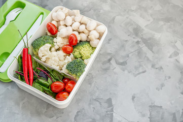 Mixed cauliflower and broccoli vegetables, baby salad, mushrooms, peppers, tomatoes and chili in lunch box on wooden background in rustic style