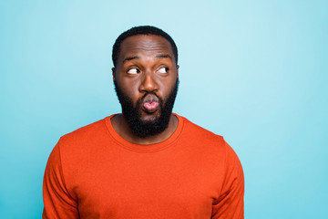 Photo of attractive dark skin guy in flirty mood sending girlfriend air kisses looking side empty space funny wear casual orange pullover isolated blue color background