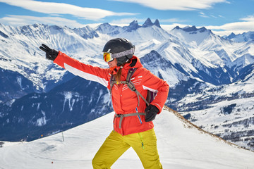 Woman skier smiling and posing at Les Sybelles ski domain, with Aiguilles d'Arves peaks in the...