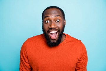 Closeup photo of attractive dark skin guy toothy beaming smiling open mouth unexpected good news positive mood wear orange jumper isolated blue color background