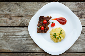 Restaurant food. Pure potatoes combined with grilled pork, decorated with cherry tomatoes. On the wooden floor.