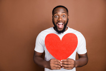 Photo of cheerful shocked stunned guy holding red heart shape with hands expressing emotions on...