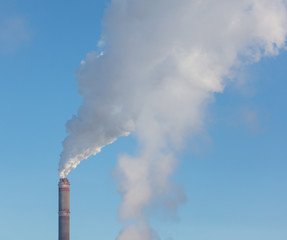 Smoke from a chimney in a factory against a blue sky