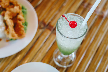 Fresh kiwi syrup and ice cube with soda and cherry on top for summer time on wooden table background.