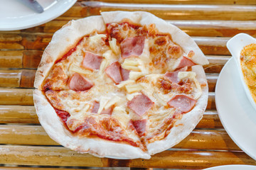 Slice of delicious hawaiian pepperoni pizza with cheese on wooden table background.