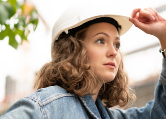 Close up portrait of a pensive and contemplative factory female employee wearing a white protective hard hat