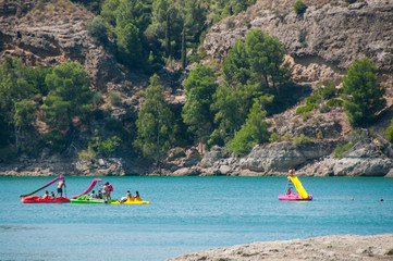 People swimming and relaxing on a lake with rocky shore. Sunny day on a lake with turquoise water. Summer vacations. Water reservoir in Spain.