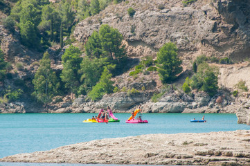 People swimming and relaxing on a lake with rocky shore. Sunny day on a lake with turquoise water. Summer vacations. Water reservoir in Spain.