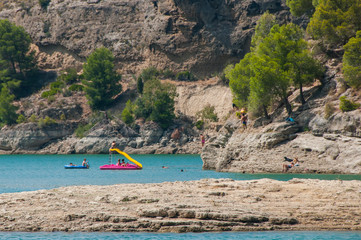 People swimming and relaxing on a lake with rocky shore. Sunny day on a lake with turquoise water. Summer vacations. Water reservoir in Spain.