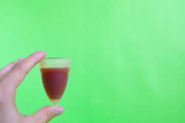 woman hand holding menstrual cup with blood on green background. space for text