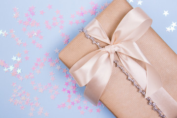 Beautiful background for holidays. Gift box with beige bow and glitter stars on a pastel blue background.