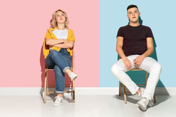 Obraz premium Young emotional man and woman in bright casual clothes posing on pink and blue background. Concept of human emotions, facial expession, relations, ad. Beautiful caucasian couple sitting dreamful.