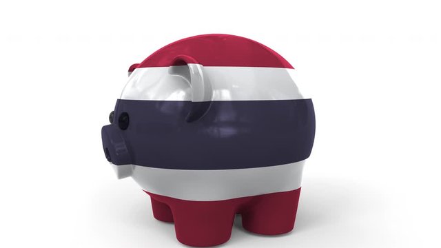 Coins fall into piggy bank painted with flag of Thailand. National banking system or savings related conceptual 3D animation