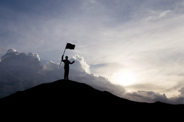 Silhouette of businessman holding a flag on top mountain, sky and sun light background. Business success and goal concept. © cofficevit
