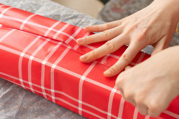 Holding down the stylish red plaid wrapping paper while she carefully wraps her husbands holiday gift