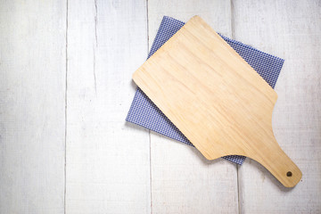 Top view of light  wooden cutting board with blue cloth on white wood table.