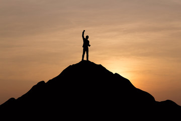 Silhouette of businessman raising his hand to celebrate success on top mountain, sky and sun light background.
