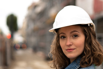 Close-up portrait of a pretty and young female factory worker wearing a white protective helmet