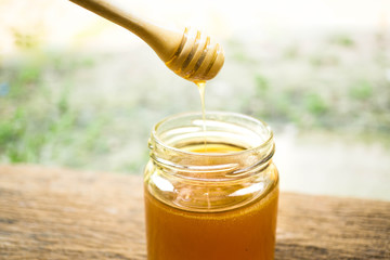 Sweet honey flowing from honey scoop in to jar.