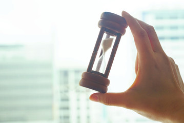 Hand hold hourglass with blur background business building