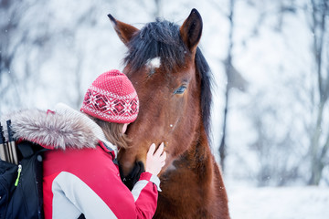 Girl with a backpack hugging with a horse in winter time. Wonderful winter weather with falling...