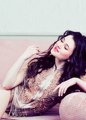 Naklejka premium young pretty brunette girl in fashion dress on sofa posing in luxury interior, lifestyle rich people concept