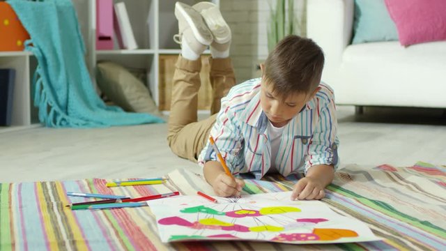 Little caucasian boy lying on floor in kids room and drawing greeting poster for Mother Day