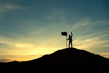 Silhouette of people and flag on top mountain, sky and sun light background. Business success and goal concept.