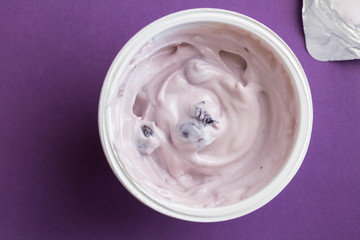 Blueberry yogurt in plastic cup with foil lid on side isolated on deep purple background
