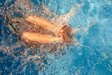 Children on vacation. A child playing under water in a pool of pure blue water. Legs sticking out of the pool. The concept of rest.