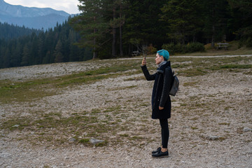 A girl with a phone stands near the forest and takes a photo. Tourist location, travel and vacation