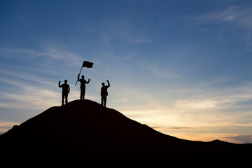 Silhouette of people are celebrating success at the top of the mountain, sky and sun light background. Team business concept.