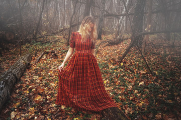 Young pretty woman in the red dress is walking in the foggy mystical forest