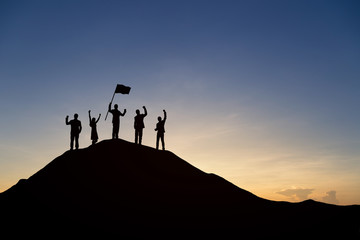 Silhouette of people are celebrating success at the top of the mountain, sky and sun light background. Team business concept.