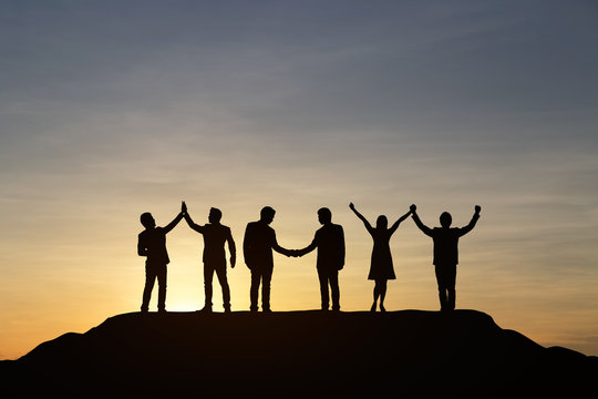 Silhouette Of People Are Celebrating Success At The Top Of The Mountain, Sky And Sun Light Background. Team Business Concept.