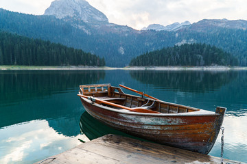 Fototapeta na wymiar Mountain lake with coniferous forest, a wooden boat and a pier in the frame. Romantic tourist place. National Park Durmitor, Montenegro, Europe.