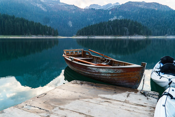 Mountain lake with coniferous forest, a wooden boat and a pier in the frame. Romantic tourist place. National Park Durmitor, Montenegro, Europe.