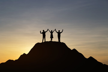 Silhouette of people are celebrating success at the top of the mountain, sky and sun light background. Team business concept.